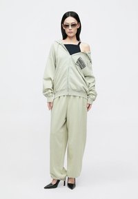 Világosszürke, oversized kapucnis pulóver, elülső cipzárral, nyomtatott logóval, széles szárú nadrággal párosítva. Sleek fekete magassarkú cipővel kiegészítve.