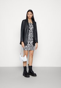 Blazer de couro preto sobre um vestido justo em preto e branco com padrões espiralados, combinado com botas pretas de cadarço e uma pequena bolsa branca.
