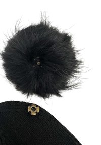 Pom-pom in pelliccia sintetica nera con lunghe e sottili ciocche sopra un tessuto a maglia nera, dotato di un attacco metallico con design circolare.