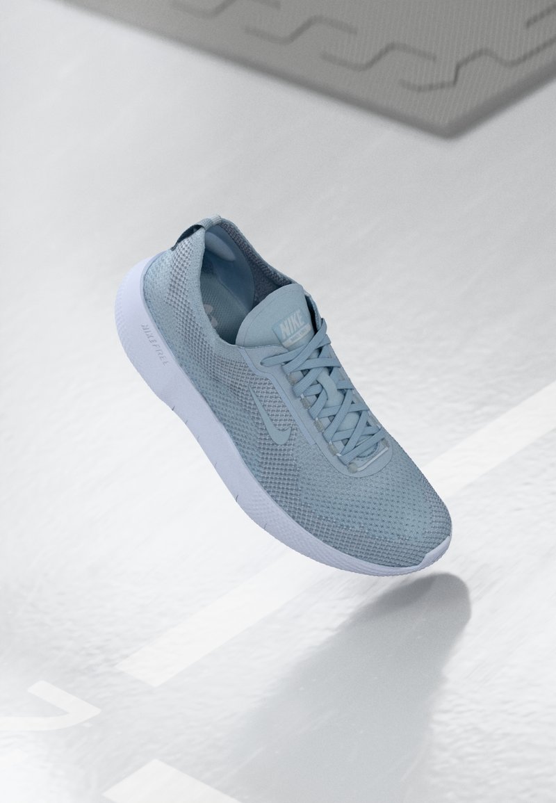 Zapatilla deportiva de color azul claro con parte superior de malla, cordones planos y suela de goma. Presenta un diseño minimalista y un sutil logotipo en el lateral.