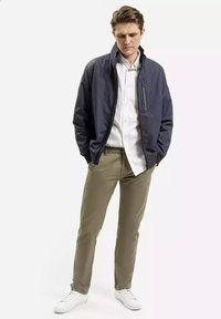 Granatowa kurtka bombowca na białej koszuli z guzikami, w połączeniu z khaki spodniami i białymi trampkami. Posiada kieszeń na zamek błyskawiczny na klatce piersiowej.