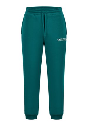 Teal joggerhousut, jotka on valmistettu pehmeästä kankaasta, joissa on joustava vyötärö ja nyöri sekä ribbireunat. "SMILODO" -logo brodeerattu eteen.