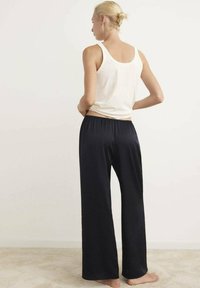Pantalones de pierna ancha de color navy con cinturilla elástica, combinados con una camiseta sin mangas blanca ajustada. Tejido suave y silueta relajada, descalza sobre una alfombra clara.