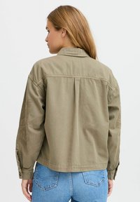 Olivovo zelená, ľahká bunda so voľným strihom, ktorá má detailné vyšívanie na rukávoch a jednoduchý design goliera.