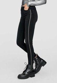 Svarta högmidjade skinny jeans med en kontrasterande silverrand på sidan, tillsammans med kraftiga svarta snörkängor.