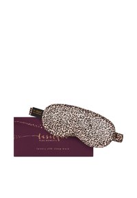 Zijden slaapmasker met luipaardprint rustend op een donkerpaarse doos met gouden decoratieve tekst en sterren.
