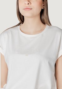 T-shirt bianco in cotone con scollo rotondo, maniche corte arrotolate e logo in rilievo "LIU JO" sopra l'anno "1995" in un delicato color pesca.