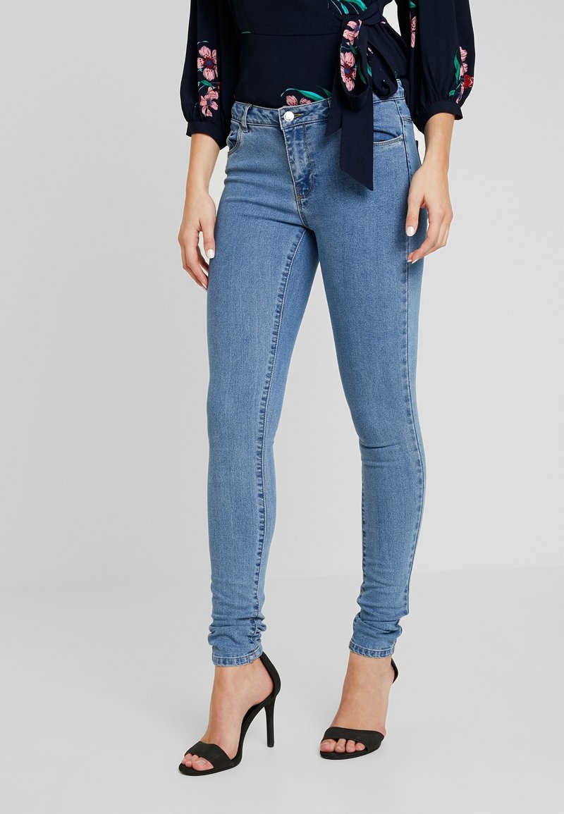 Vaqueros ajustados de mezclilla en un tono azul claro con un diseño clásico de cinco bolsillos, con una cintura de altura media y un ligero desgastado, combinados con tacones negros.