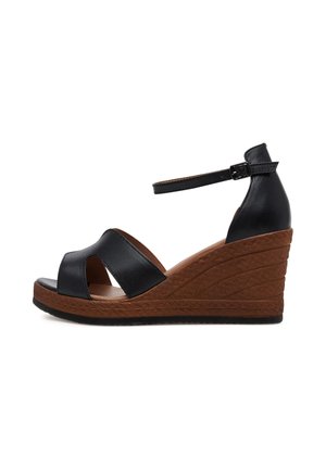 Sandalias cuña de cuero negro con punta abierta, con un diseño entrecruzado en la parte delantera y un tacón cuña marrón texturizado. Correa ajustable en el tobillo.