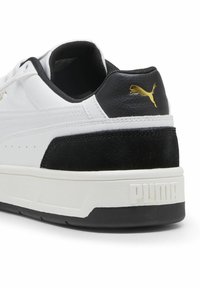 Adidași albi cu toc din suede negru și accente negre, având o talpă texturată albă și un logo Puma aurit în spate.