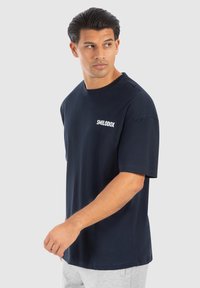 Camiseta de manga corta azul marino hecha de algodón, con un logo blanco en el lado izquierdo del pecho, cuello redondo y un corte relajado.