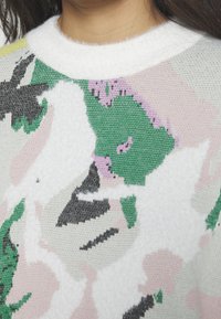 Maglione a maglia con colletto bianco, tessuto testurizzato e un motivo astratto multicolore in verde, rosa, nero e bianco.