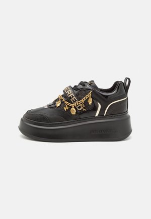 Czarny sneaker na platformie z złotym łańcuszkiem i zawieszkami, z markowym paskiem i wyściełanym kołnierzem na białym tle.