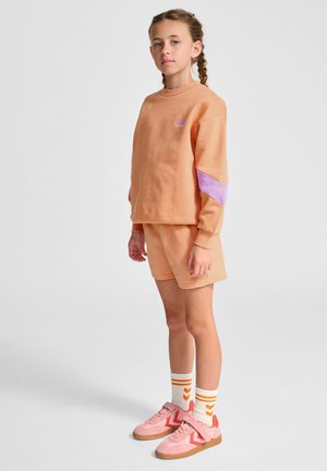 Lys orange sweatshirt med lilla detaljer, parret med matchende shorts. Båret med lyserøde sneakers og hvide sokker med orange striber.