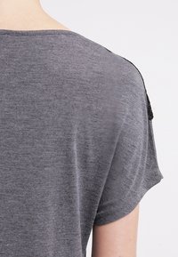 Szary krótki rękaw z luźnym krojem. Tkanina wydaje się miękka z delikatną fakturą, z czarnymi akcentami na szwach ramion.