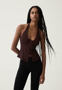 Top bordeaux senza maniche con scollo a V profondo e design con lacci frontali. Presenta righe verticali e orlo svasato. Abbinato a pantaloni skinny neri.