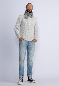 Suéter de punto en gris claro, jeans de corte relajado en azul claro, zapatillas altas negras con suelas blancas y una bufanda gris.