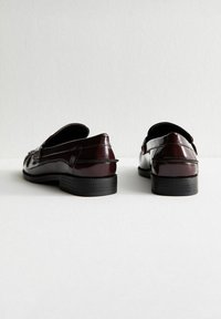 Mocassini bordeaux lucidi con tacco nero basso, caratterizzati da cuciture dettagliate e design a punta arrotondata. Finitura in pelle verniciata liscia.