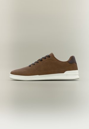 Brauner Sneaker mit niedrigem Schaft, perforierten Seiten, dunklen Schnürsenkeln, dunklem Fersenakzent und weißer Gummisohle vor neutralem Hintergrund.