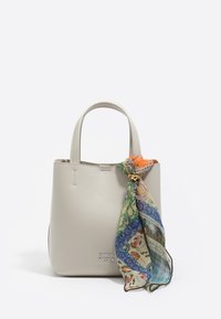 Bolso pequeño de piel beige con doble asa, adornado con un pañuelo colorido de paisley anudado en un lado y logo plateado de "Bimba y Lola".