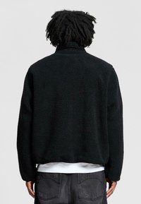 Mustikka turkkitekstuuri takki korkealla kauluksella, rento istuvuus ja pitkät hihat. Vaatteen päällä valkoinen paita, yksinkertainen muotoilu ilman näkyviä logoja.