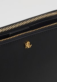 Portefeuille zippé en cuir noir avec des quincailleries dorées, un logo bien visible et une texture lisse.
