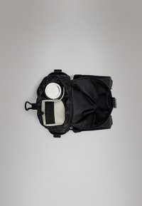 Saco de tecido preto com abertura com zíper, contendo um recipiente circular e uma bolsa retangular clara com uma alça preta.