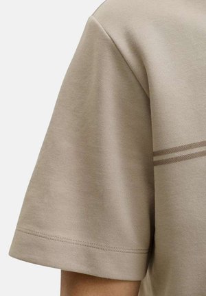 Chemise beige à manches courtes avec deux fines rayures horizontales sur le haut du bras et un ourlet proprement cousu.