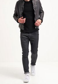 Svart läderjacka, svart tröja, mörka jeans och vita sneakers. Jackan har dragkedjestängning; jeansen är slim-fit.