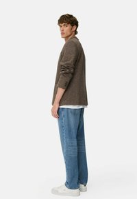 Brun tekstureret langærmet skjorte over en hvid t-shirt, parret med lyseblå løstsiddende jeans og hvide sneakers.