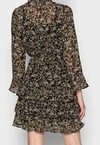 Vestido negro semitransparente con estampado floral, con volantes en capas, mangas largas y cinturón de lazo. Presenta pequeños detalles florales en blanco y rosa.
