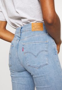 Vaqueros de tiro alto azul claro fabricados en denim, con una etiqueta de cuero que lleva el logo de la marca y un característico bordado en los bolsillos traseros.
