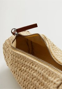 Bolso de cosméticos de paja natural tejida con un tirador de cremallera de cuero marrón y una cremallera dorada. Interior forrado en tela suave, detalles visibles.