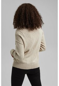Maglione lavorato a maglia beige con vestibilità comoda, orlo e polsini a coste. Mostra un tessuto testurizzato sul retro, abbinato a pantaloni neri.