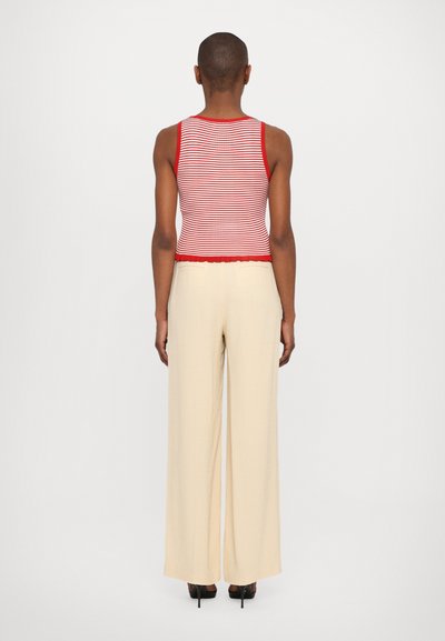 Débardeur ajusté à rayures rouges et blanches avec un ourlet en forme de vagues, associé à un pantalon large crème, mettant en avant une texture de tissu lisse.