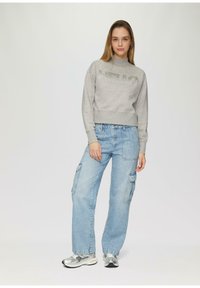 Grijze sweatshirt met "HELLO" opdruk, gecombineerd met lichtblauwe cargobroeken met zijzakken. Zilveren sportschoenen maken de look af.