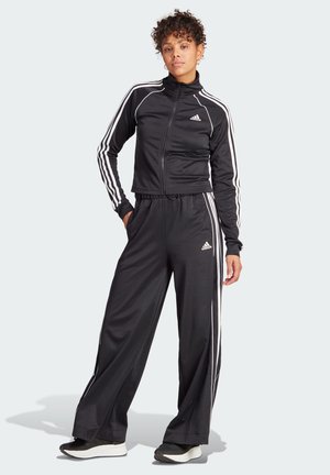 Tuta sportivo nero realizzato in tessuto liscio, con strisce bianche Adidas lungo i lati e una giacca con zip e colletto alto.
