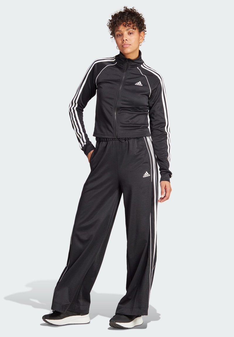 Black athletic tracksuit made of smooth fabric, featuring white Adidas stripes along the sides and a zip-up jacket with a high collar.
