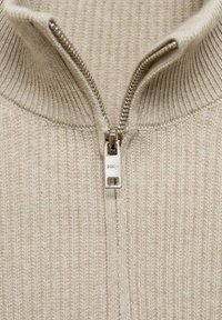 Beige ribbed knit zip-up pullover with a silver zipper and high collar. The fabric appears soft with a fine texture throughout.