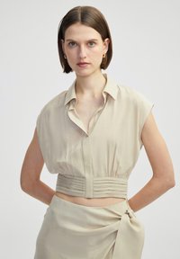 Beige cropped blouse met korte mouwen, met een kraag aan de halslijn en geplooide taille detail. Gladde stof en een ontspannen pasvorm.