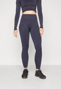 Dark navy fitted leggings with a high waistband and ribbed texture, paired with a matching long-sleeve crop top. Black athletic shoes.