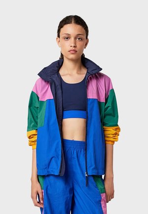 Giacca a vento colorata con sezioni blu, rosa, verde e giallo. Materiale leggero con colletto rialzato e chiusura con zip.
