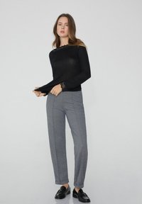 Schwarzes Langarmshirt mit Spitzenakzenten am Ausschnitt und an den Bündchen, kombiniert mit grauen karierten Anzughosen und schwarzen Slippern.