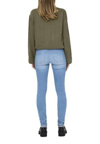 Maglione cropped verde oliva abbinato a jeans skinny azzurri chiari. I jeans presentano un classico design a cinque tasche e cuciture sottili. Scarpe con plateau nere completano il look.