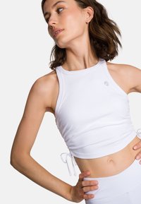 Witte geribbelde cropped top met een hoge halslijn en verstelbare zijkanten. Beschikt over een subtiele logo en een aansluitende silhouet. Glad, rekbaar materiaal.