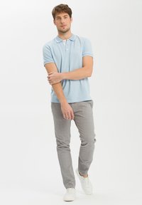 Jasnoniebieska bawełniana koszulka polo z kontrastującym jasnoniebieskim kołnierzykiem i mankietami, sparowana z szarymi teksturowanymi spodniami i białymi sneakersami.
