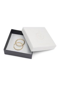 Goldene Creolen mit strukturiertem Design, präsentiert in einer weiß-schwarzen Geschenkschachtel, ausgekleidet mit grauem Stoff.