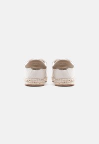 Λευκά πάνινα αθλητικά με μπεζ δερμάτινες λεπτομέρειες, σόλες από τζούτ σε στυλ εσπαντρίγια και στρογγυλεμένο σχέδιο μυτού. Λογότυπο στη φτέρνα.