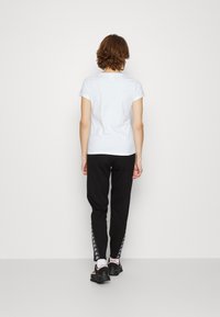 Bílý tričko s krátkým rukávem, spárované s černými kalhotami se stranovými logovými pruhy. Černé boty outfit doplňují. Jednoduchý a ležérní design.