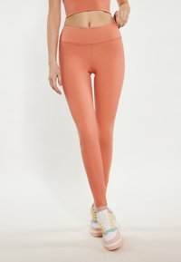 Pfirsichfarbene Leggings mit hoher Taille, hergestellt aus glattem, dehnbarem Stoff. Verfügt über ein nahtloses Design für zusätzlichen Komfort und eine enganliegende Silhouette.